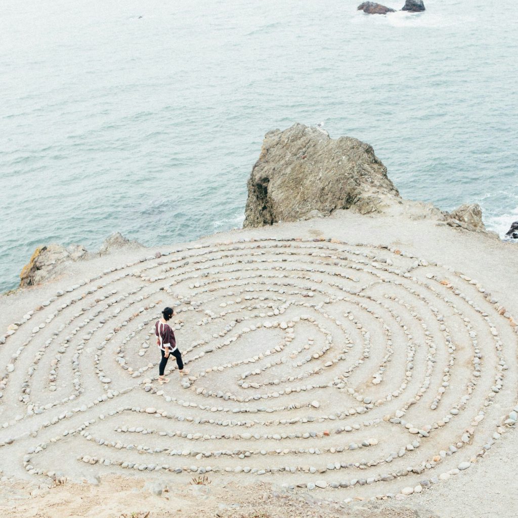 Eine Person geht durch ein mit kleinen Steinen ausgelegtes Labyrinth am Meer.