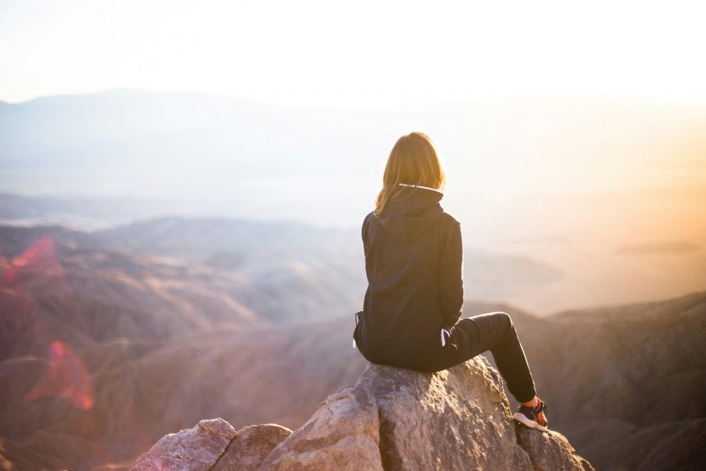 Eine Frau sitzt auf einem Felsen und schaut in das Bergpanorama.