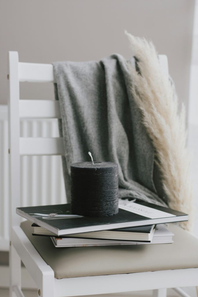 Auf einem weißen Stuhl liegen Bücher und Notizbücher übereinandergestapelt. Darauf steht eine Kerze.