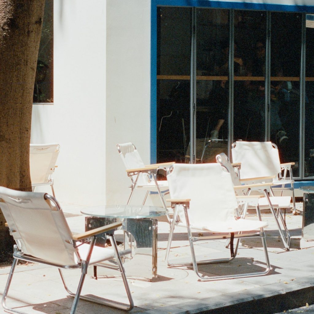 Fünf weiße Stühle vor einem großen Fenster eines Straßencafés.